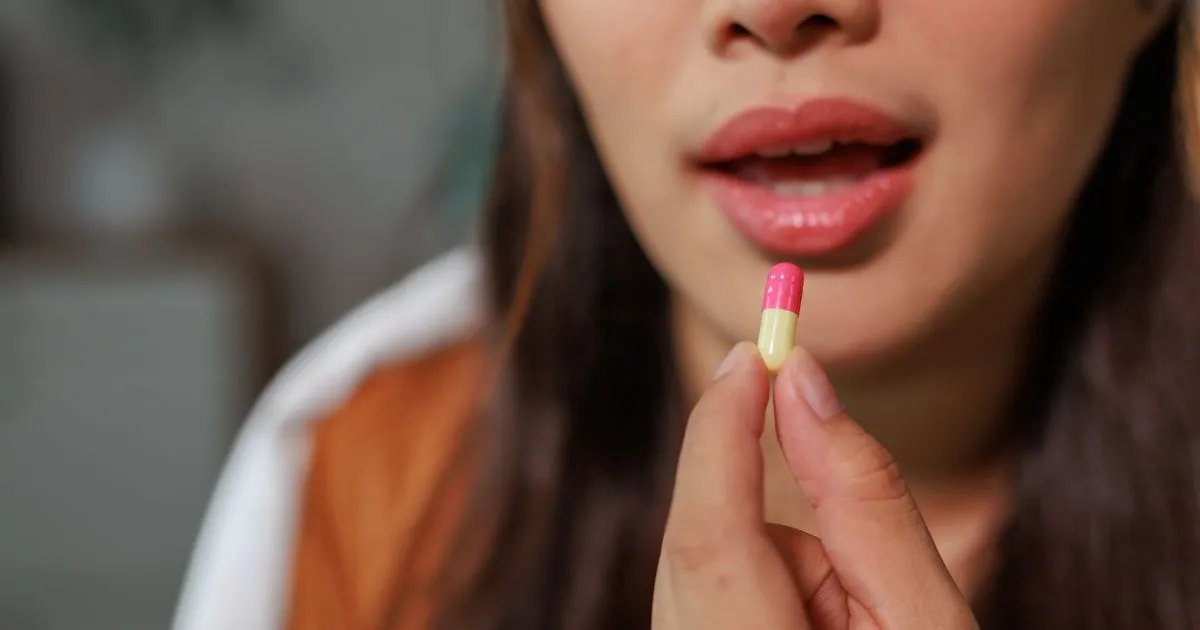 A woman holding a pink and yellow capsule for oral vitamin therapy in Basking Ridge, NJ